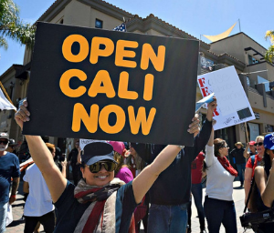 Woman holding a sign that says "OPEN CALI NOW"